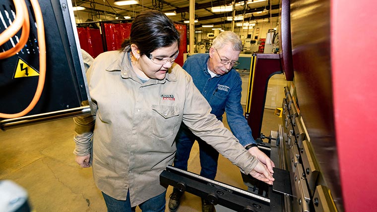 A student and professor use a piece of machinery in a welding lab.