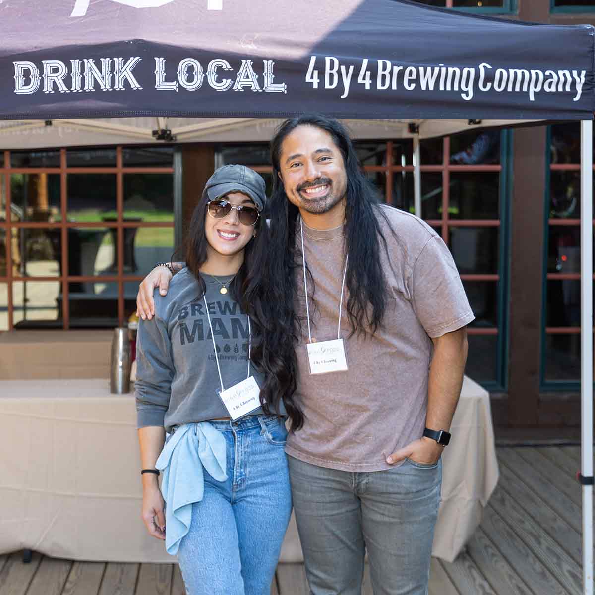 A couple pose together in front of a 4 By 4 Brewing Company tent. 
