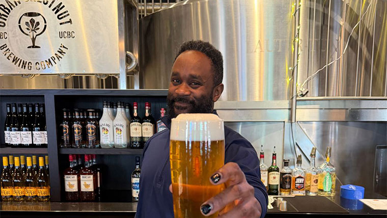 Bartender at Urban Chestnut behind the counter, holding up a glass full of beer.