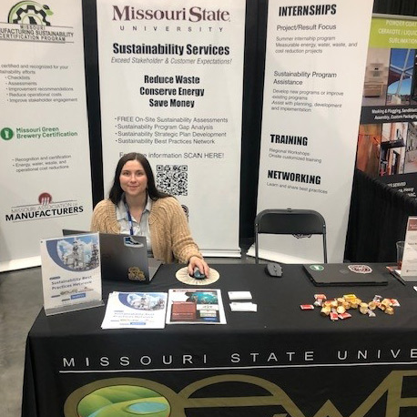 An OEWRI employee seated at an information booth during a community event.